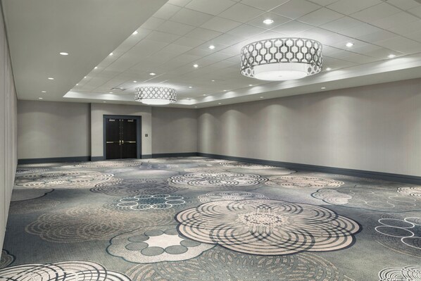 A spacious room with a patterned carpet, recessed ceiling lights, and a door.