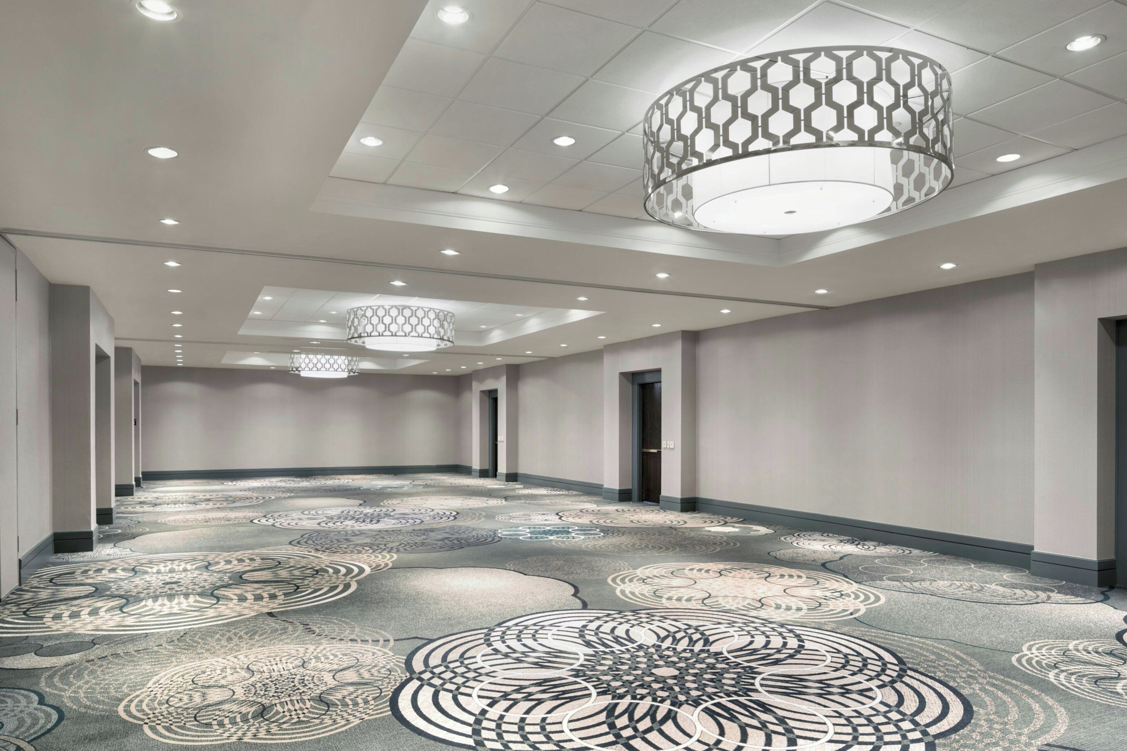 A spacious hotel corridor with patterned carpet, recessed lighting, and decorative ceiling fixtures.