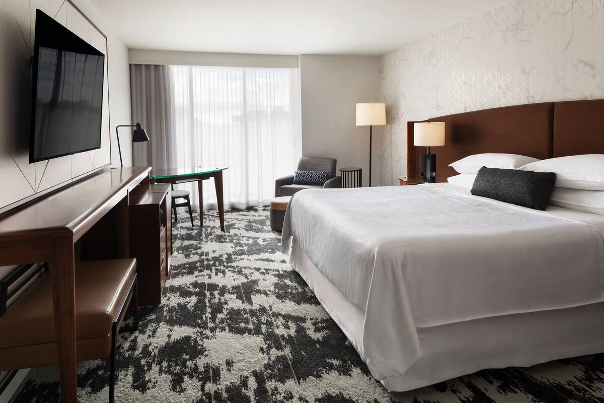 Una habitación de hotel con una cama grande, un escritorio con silla, un televisor y una lámpara.