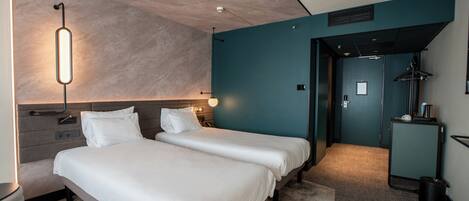 Habitación de hotel con dos camas, un escritorio y un baño visible a través de una puerta abierta.