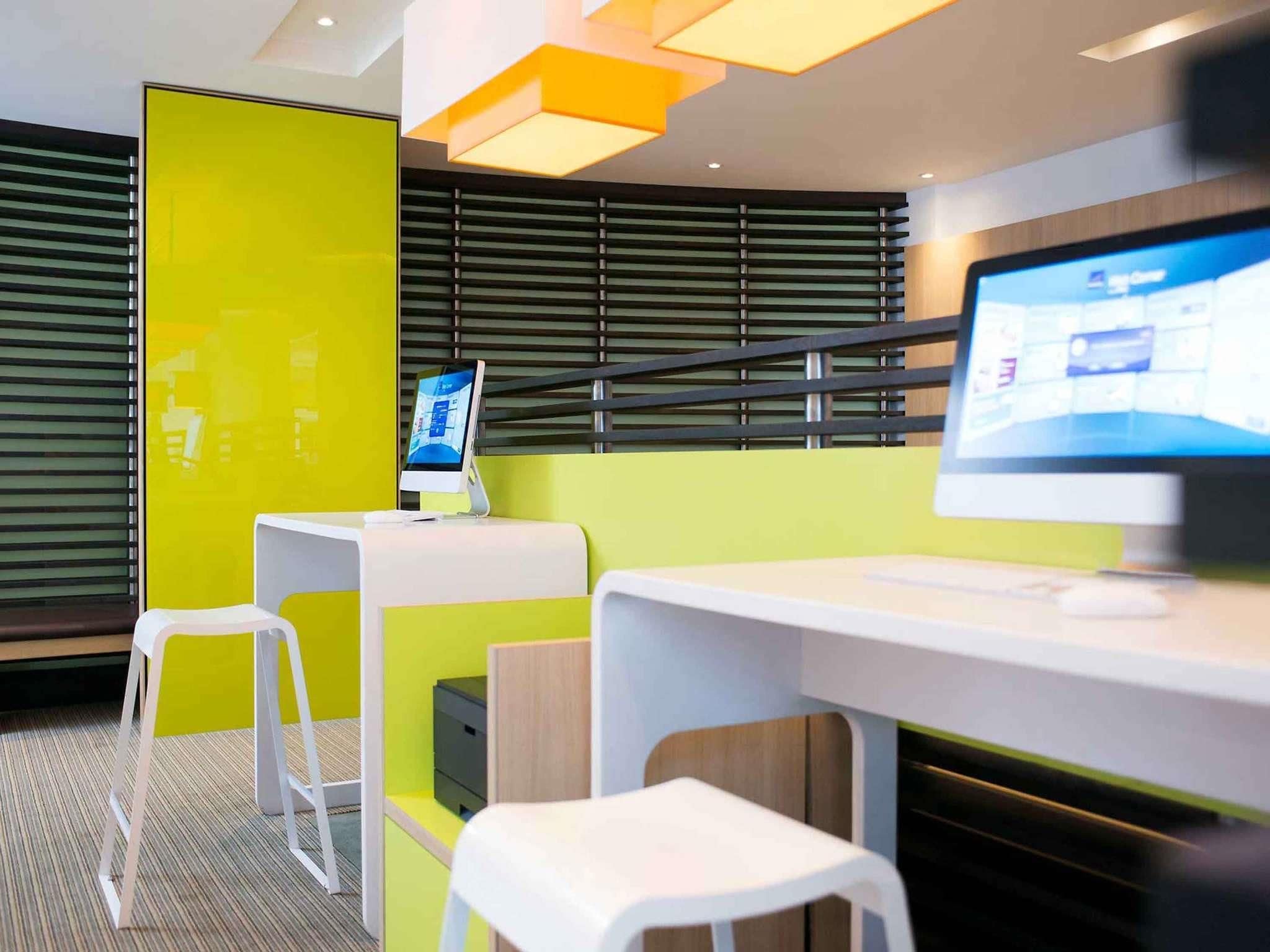 A modern, brightly lit room with a computer monitor, two white stools, and a yellow accent wall.