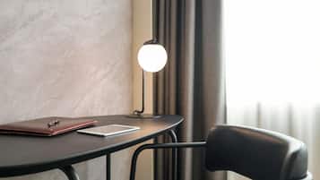 Una mesa con una computadora portátil, un cuaderno, un bolígrafo, una lámpara y una silla en una habitación con pared texturizada y cortinas.