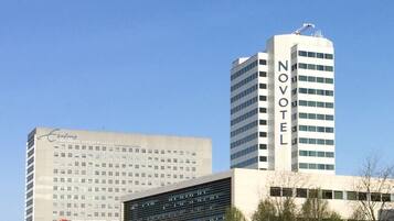 A modern hotel with a prominent 'NOVOMATIC' sign, surrounded by a well-maintained grassy area and other buildings in the background.