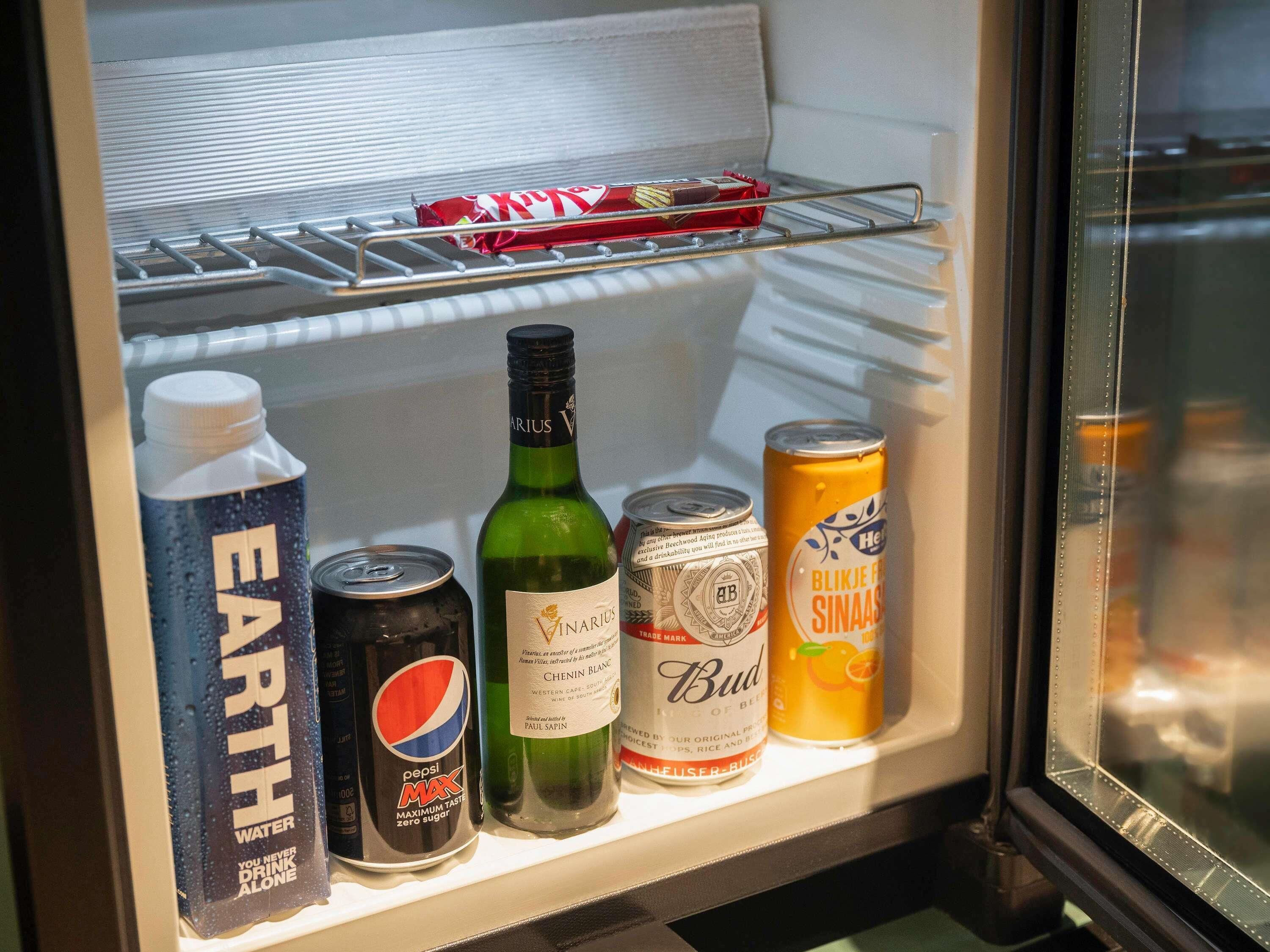 A refrigerator containing a bottle of water, a can of Pepsi Max, a bottle of Budweiser, and a can of Heineken.