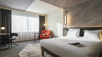 A modern hotel room with a large bed, a desk, a chair, and a lamp.