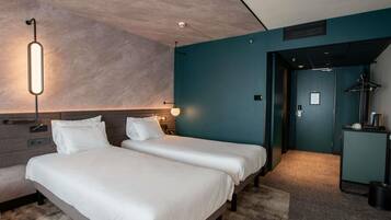 A hotel room with two beds, a desk, a chair, a lamp, and a door leading to another room.
