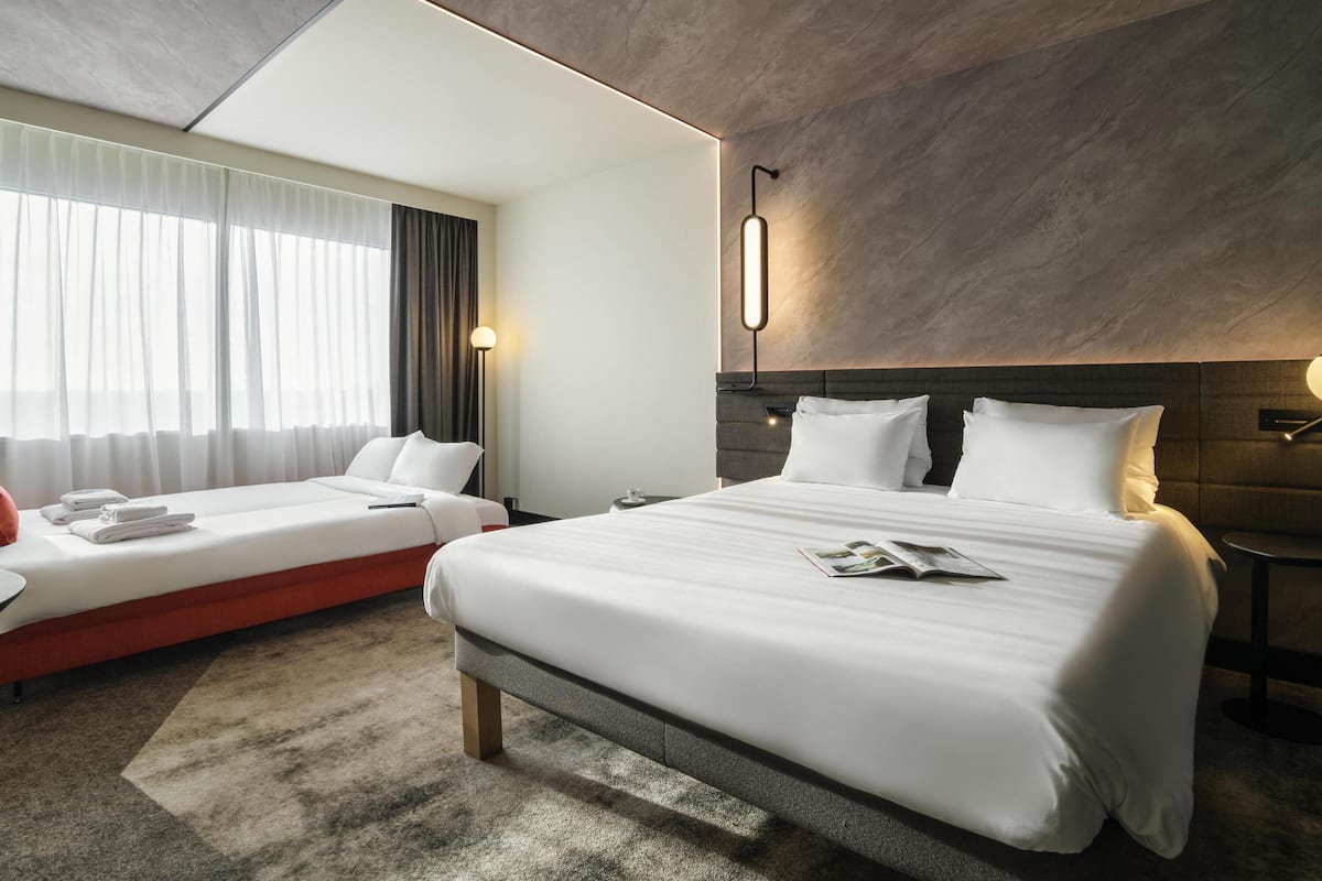 A modern hotel room with a large bed, a smaller bed, and a sofa.