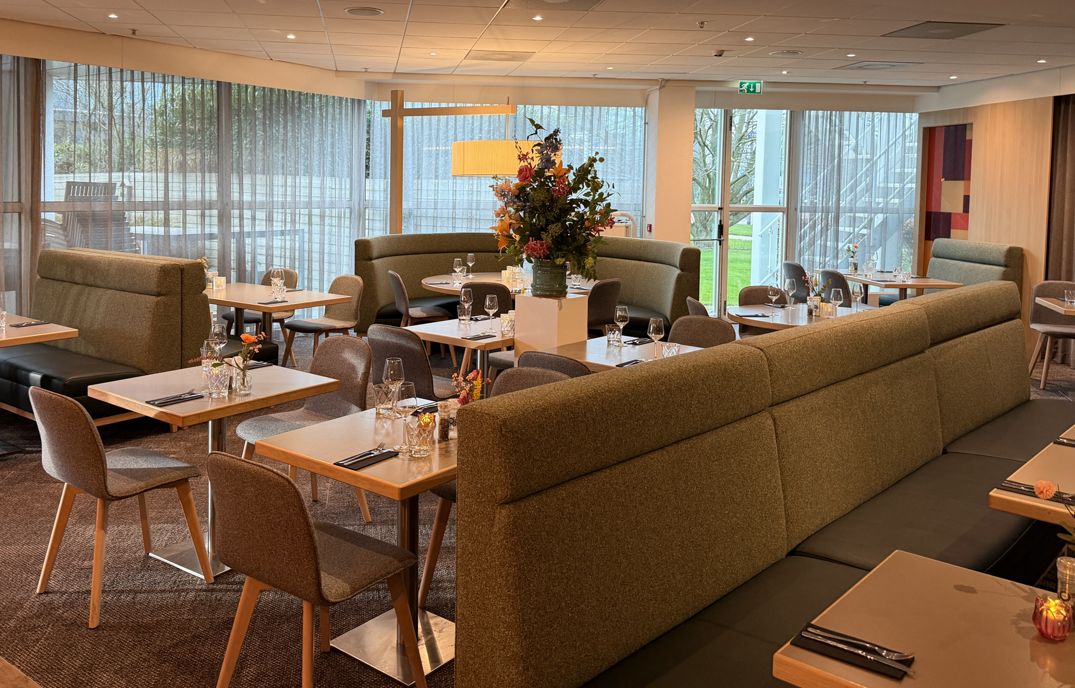 A modern restaurant with booths and tables, large windows, and a central floral arrangement.