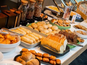 Buffet com diversos pães, doces e acompanhamentos.