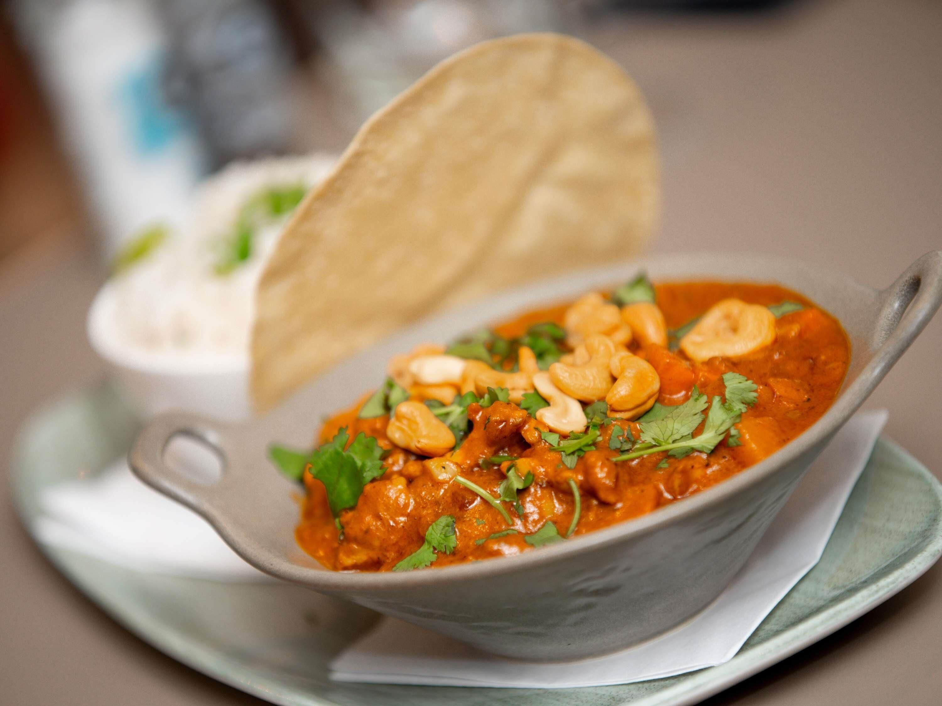 A bowl of curry with cashew nuts and cilantro, accompanied by a piece of flatbread on a plate.