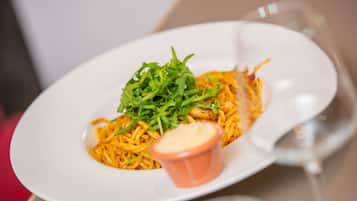 Une assiette blanche contenant des nouilles, des légumes verts et un petit bol de sauce, posée sur une table.