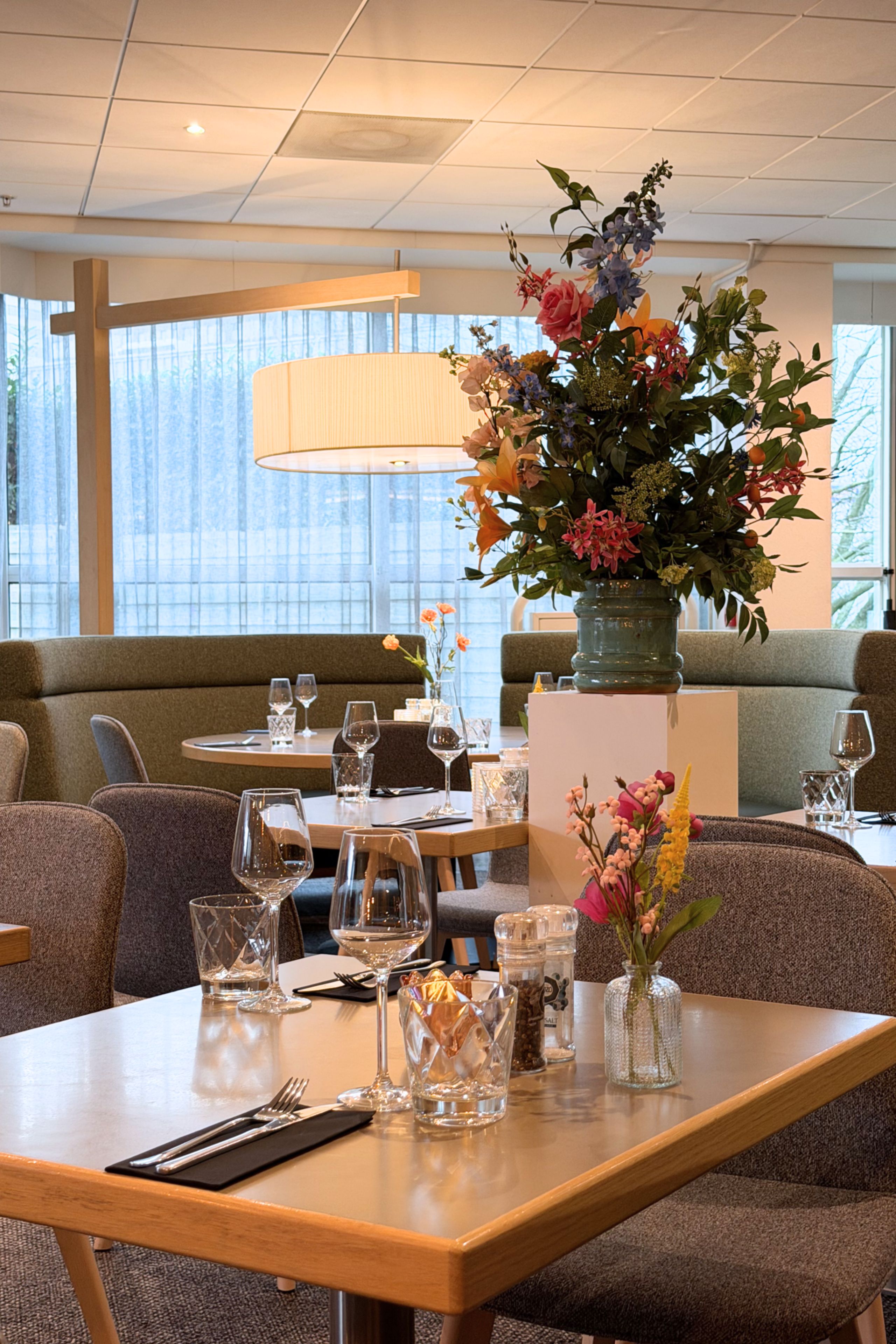 A restaurant interior with a dining table set for two, a vase of flowers, and a seating area with a sofa and chairs.
