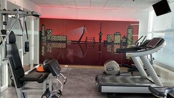 Un gimnasio con equipo de ejercicio, un mural de paisaje urbano y un proyector en el techo.