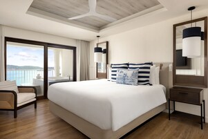 A hotel room with a large bed, a chair, a nightstand, a mirror, and a view of the ocean.