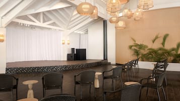 An indoor venue with a stage, black wicker chairs, and hanging wicker lamps.