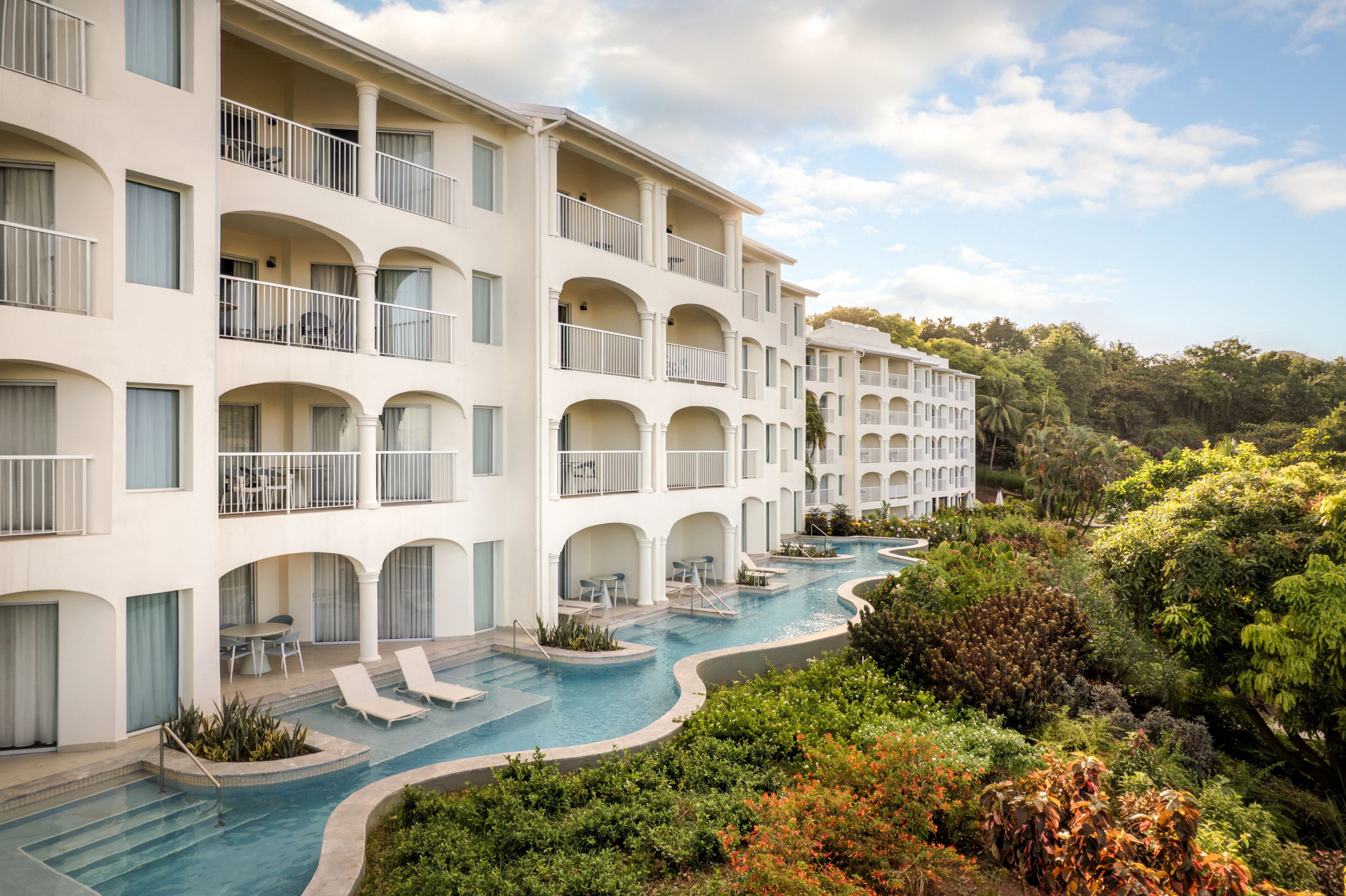 A multi-story hotel with balconies, a swimming pool, and lush greenery.