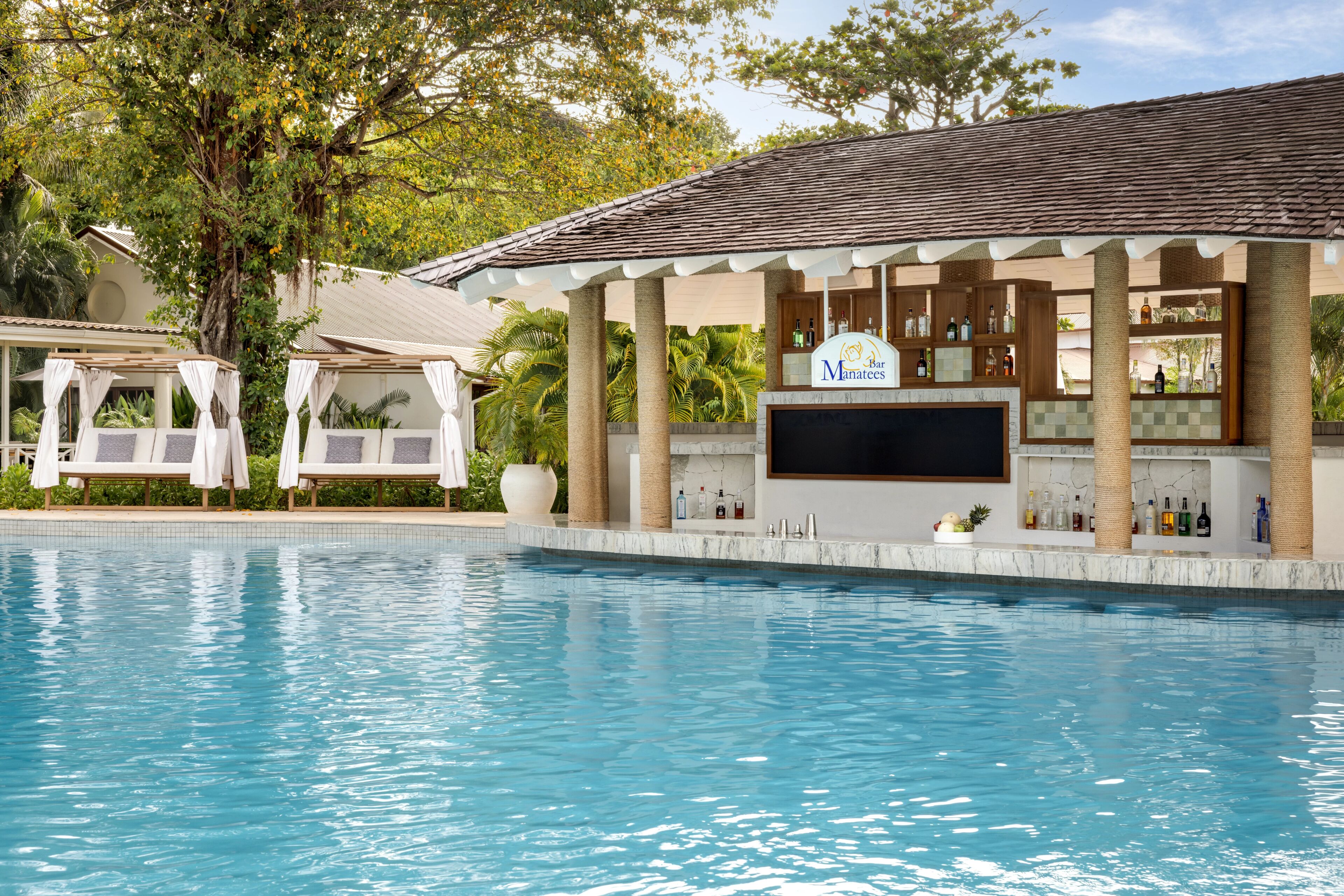 A poolside bar with a TV, bar stools, and a sign reading 'Bar Maratones.'
