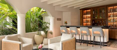 A bar area with stools and a bar counter, a seating area with chairs and a round table, and a large potted plant.