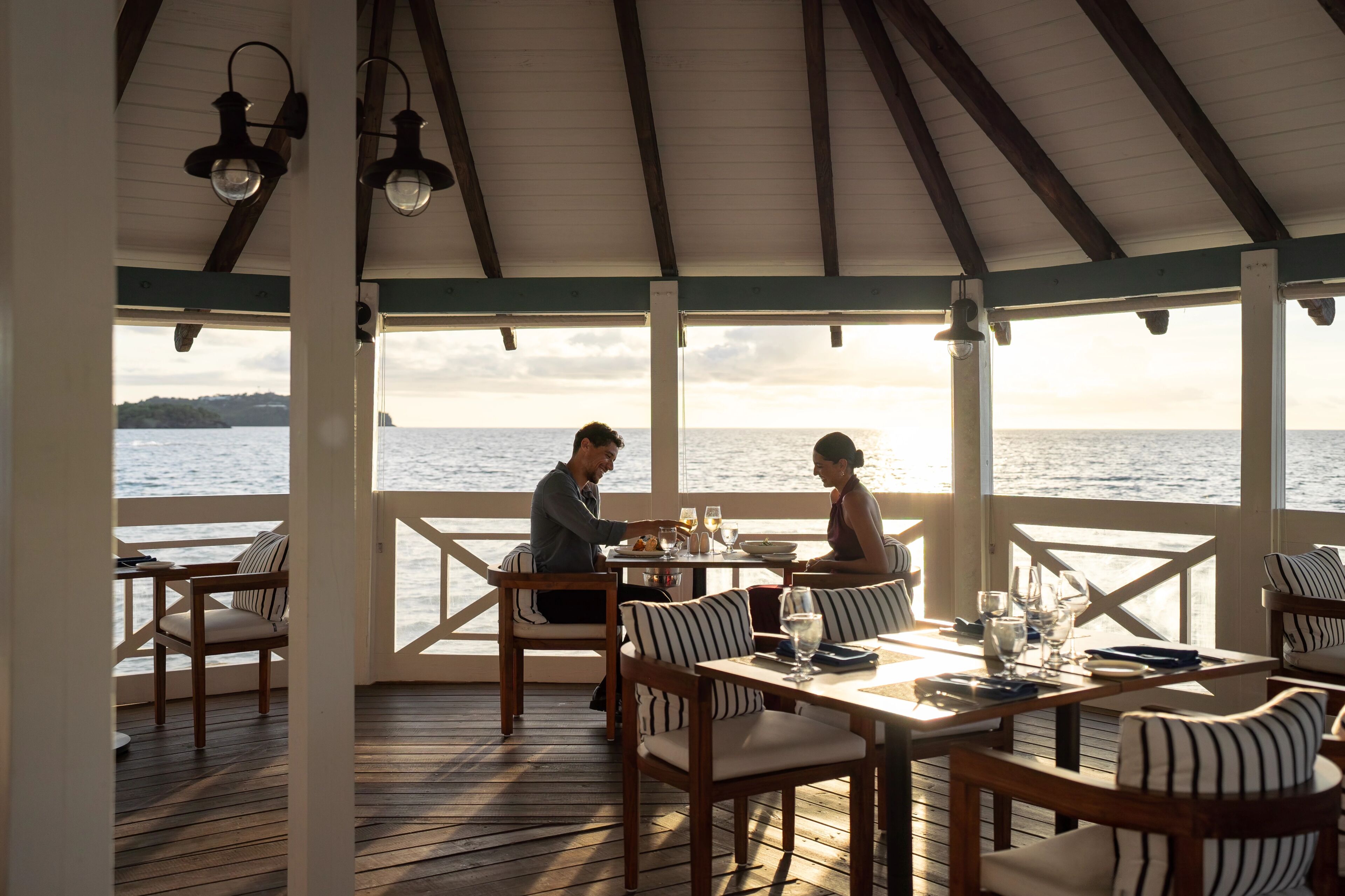 Un espace extérieur abrité, aménagé pour les repas, avec des meubles en bois et une vue sur la mer.