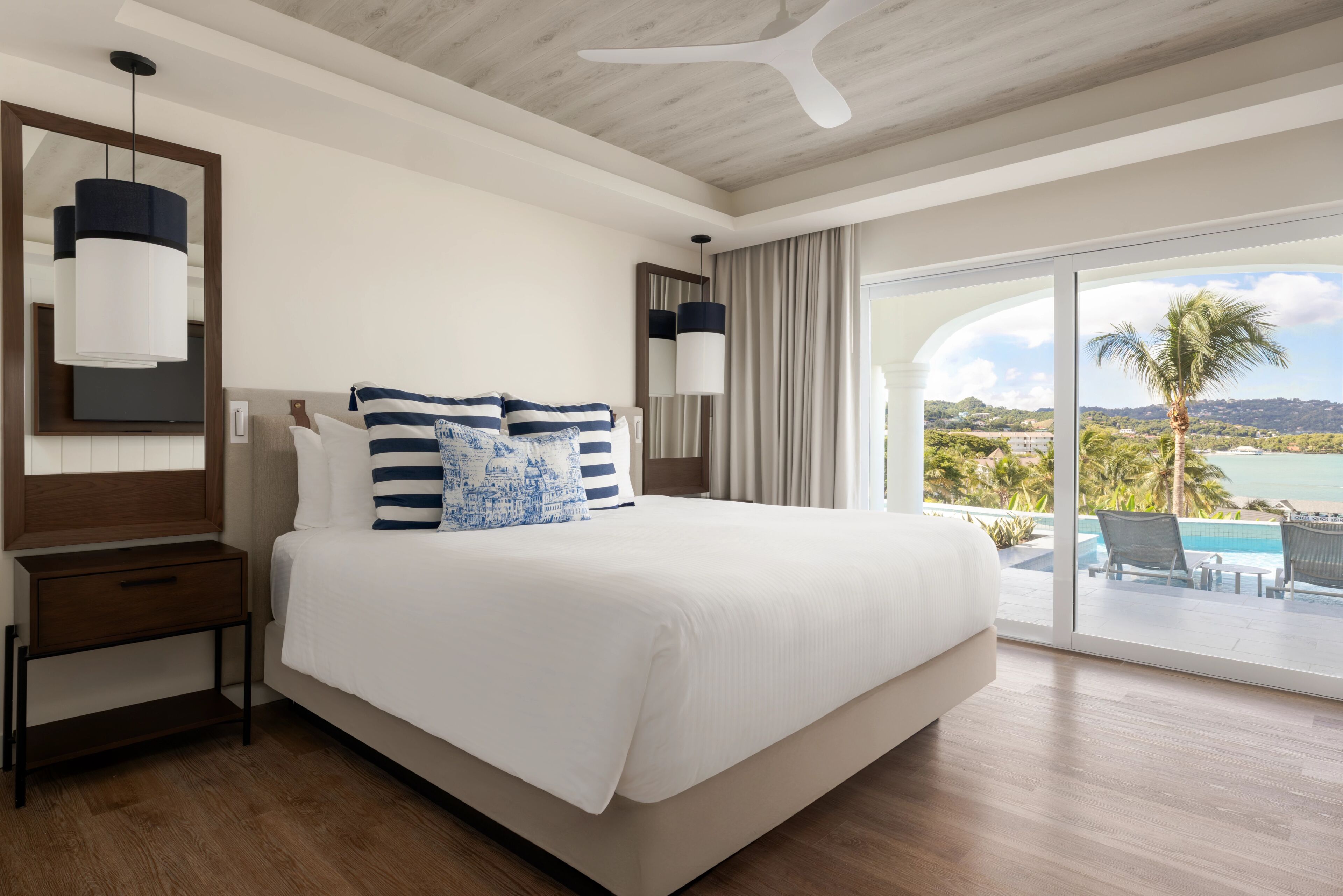 Una habitación de hotel con una cama grande, una mesita de noche, un espejo y vista al océano.