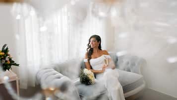 Una persona sentada en un sofá gris en una habitación con cortinas traslúcidas y un arreglo floral.