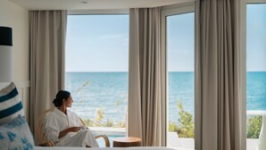 Ein Zimmer mit großem Fenster, einem Bett, einem Sessel und einem kleinen runden Tisch.