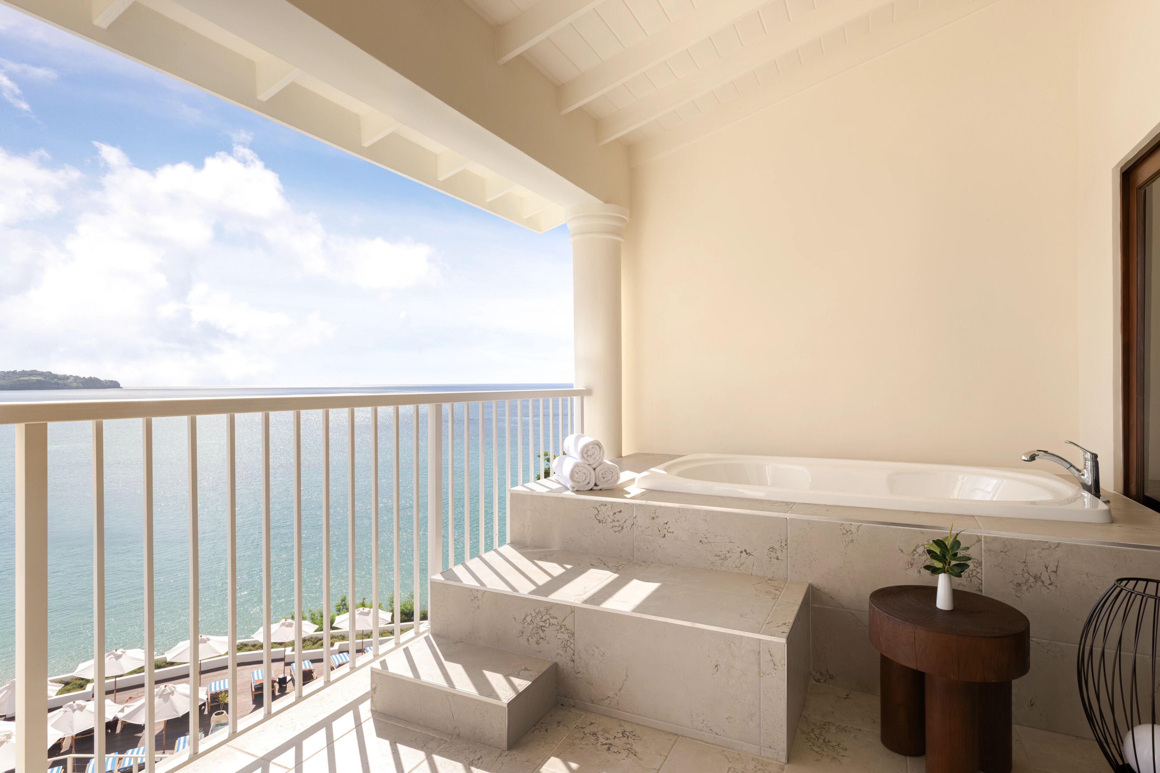 Un balcon avec vue sur la mer, une baignoire et une petite table avec une plante.