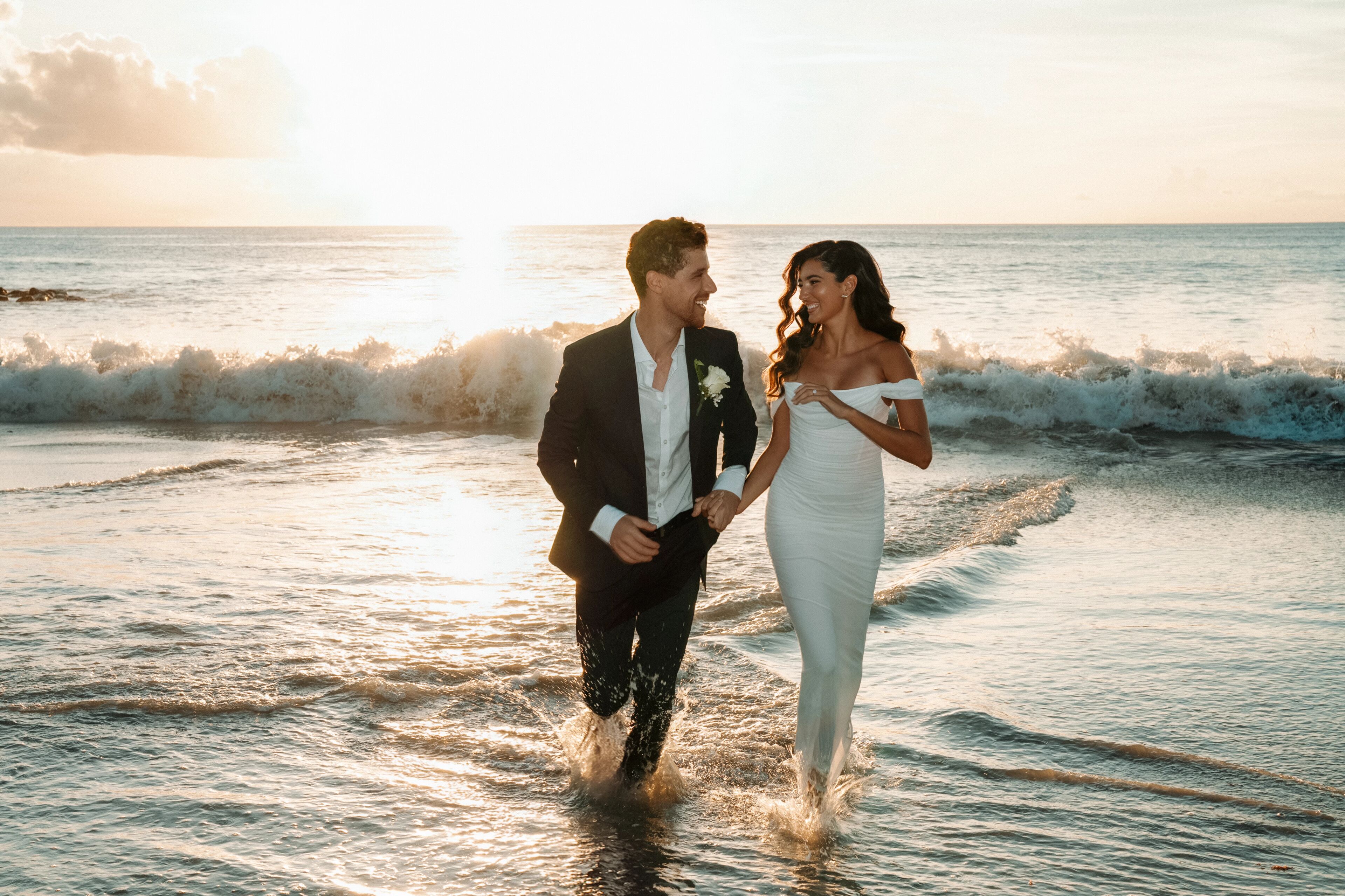 A couple walking on a beach at sunset.