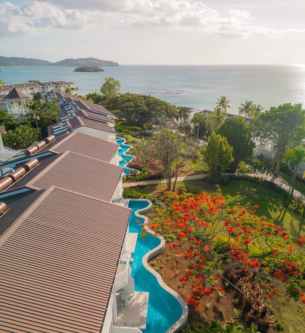 A resort with a swimming pool, a view of the sea, and tropical landscaping.
