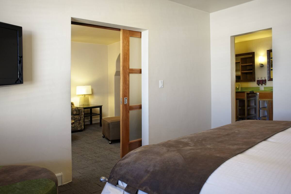 A hotel room with a bed, a desk with a lamp, and a kitchenette.