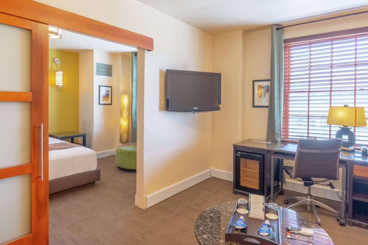 A hotel room with a bed, a desk, a chair, a television, and a window with blinds.