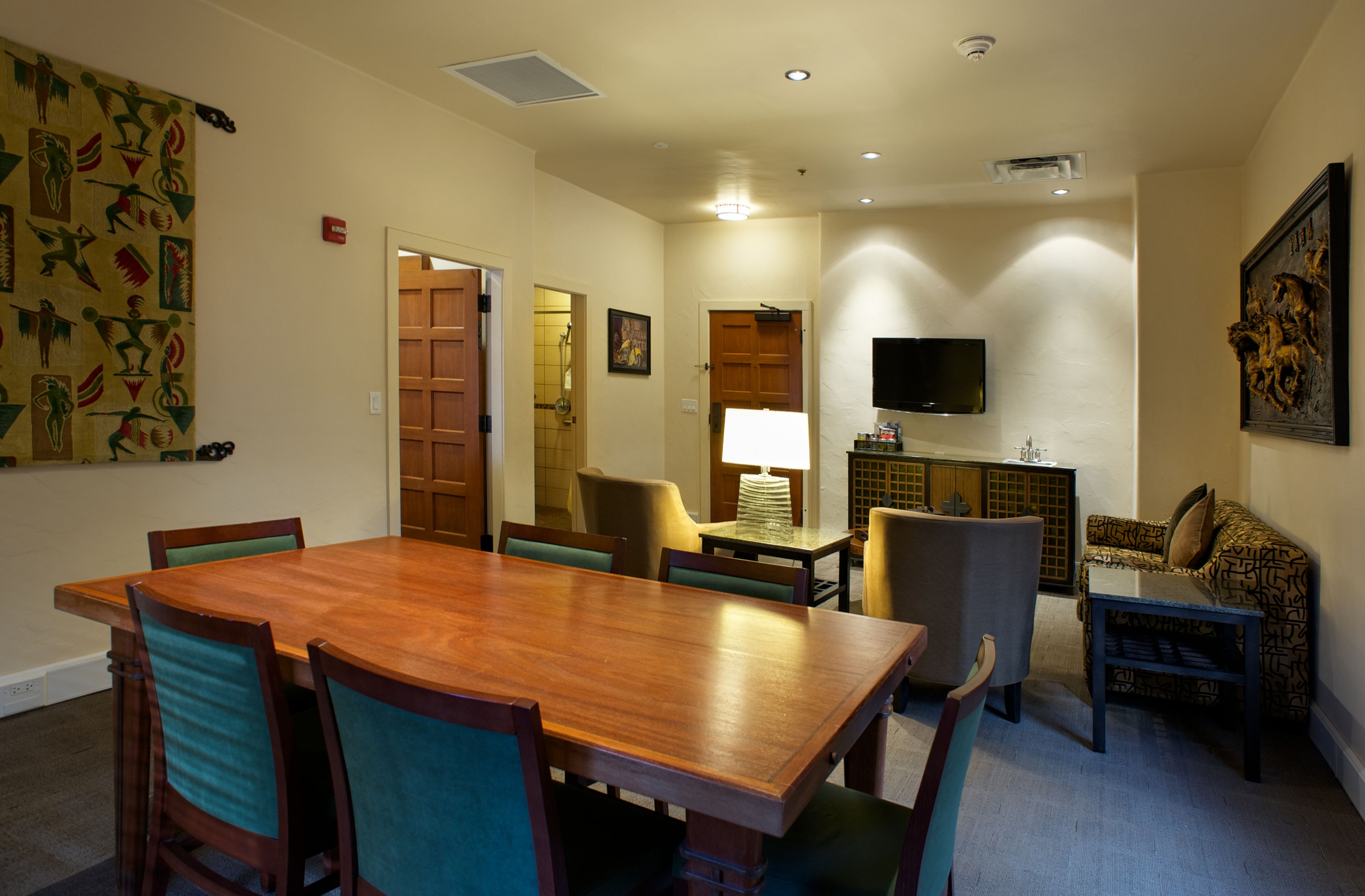 A dining area with a wooden table and chairs, a television, and a patterned wall hanging.