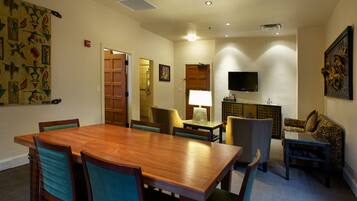 A dining area with a wooden table and chairs, a television, and a patterned wall hanging.