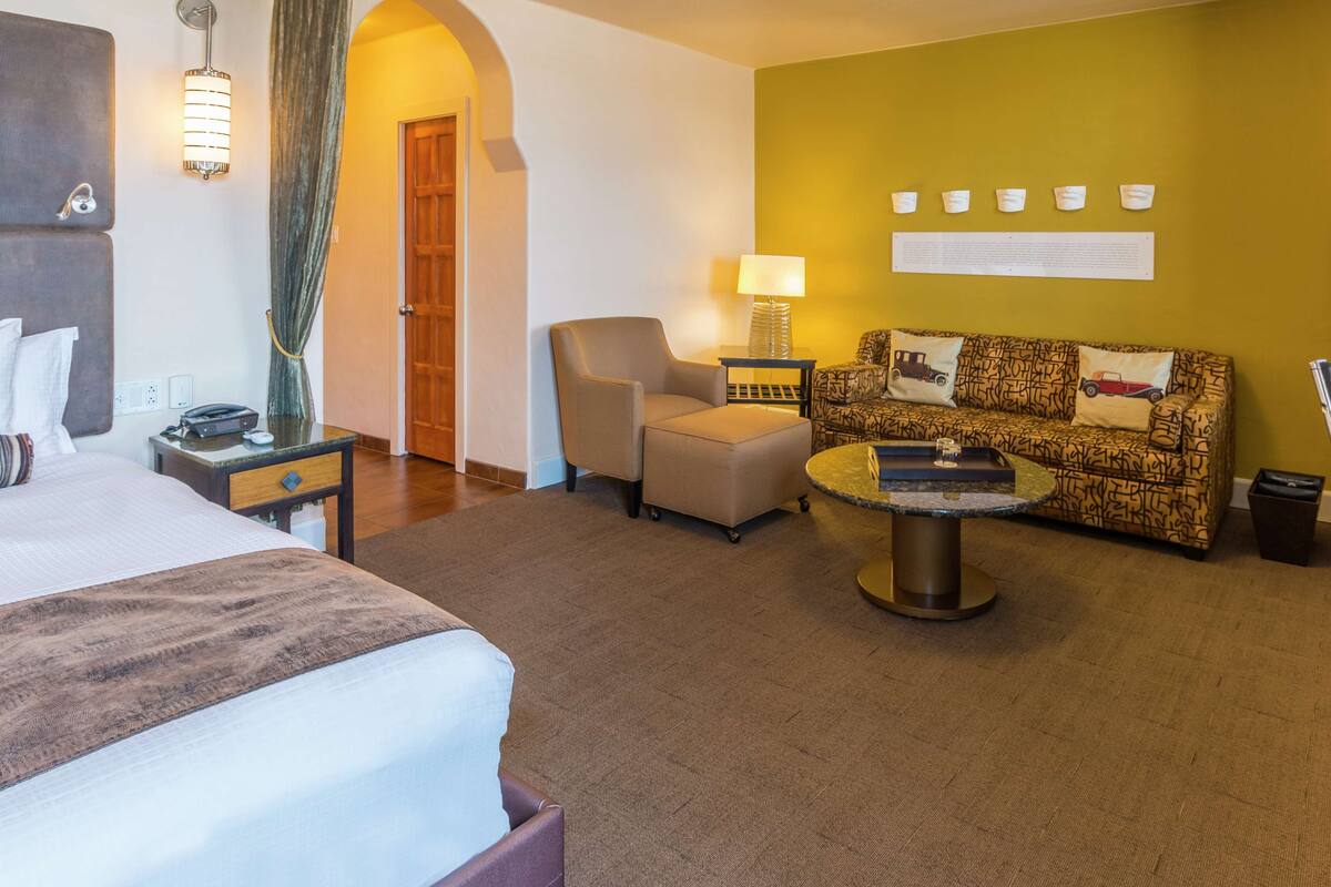 A hotel room with a bed, a sofa, a small table, a lamp, and a decorative wall piece.