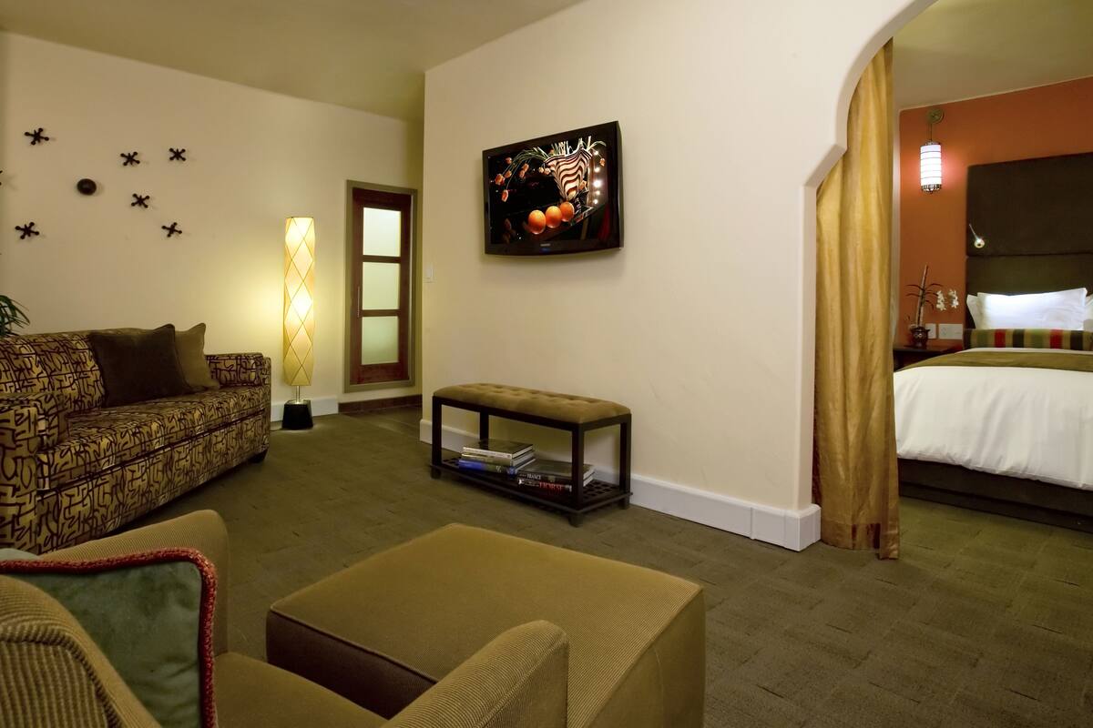 A hotel room with a sofa, a small table, a bed, and a wall-mounted TV.