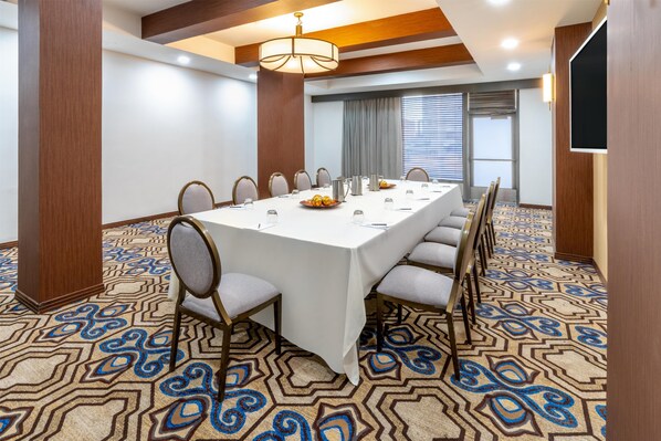 Un salón de conferencias con una larga mesa, sillas, una araña y alfombra estampada.
