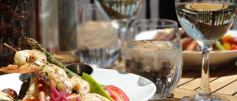A dining table with a plate of seafood, a glass of white wine, and a bottle of sauce.