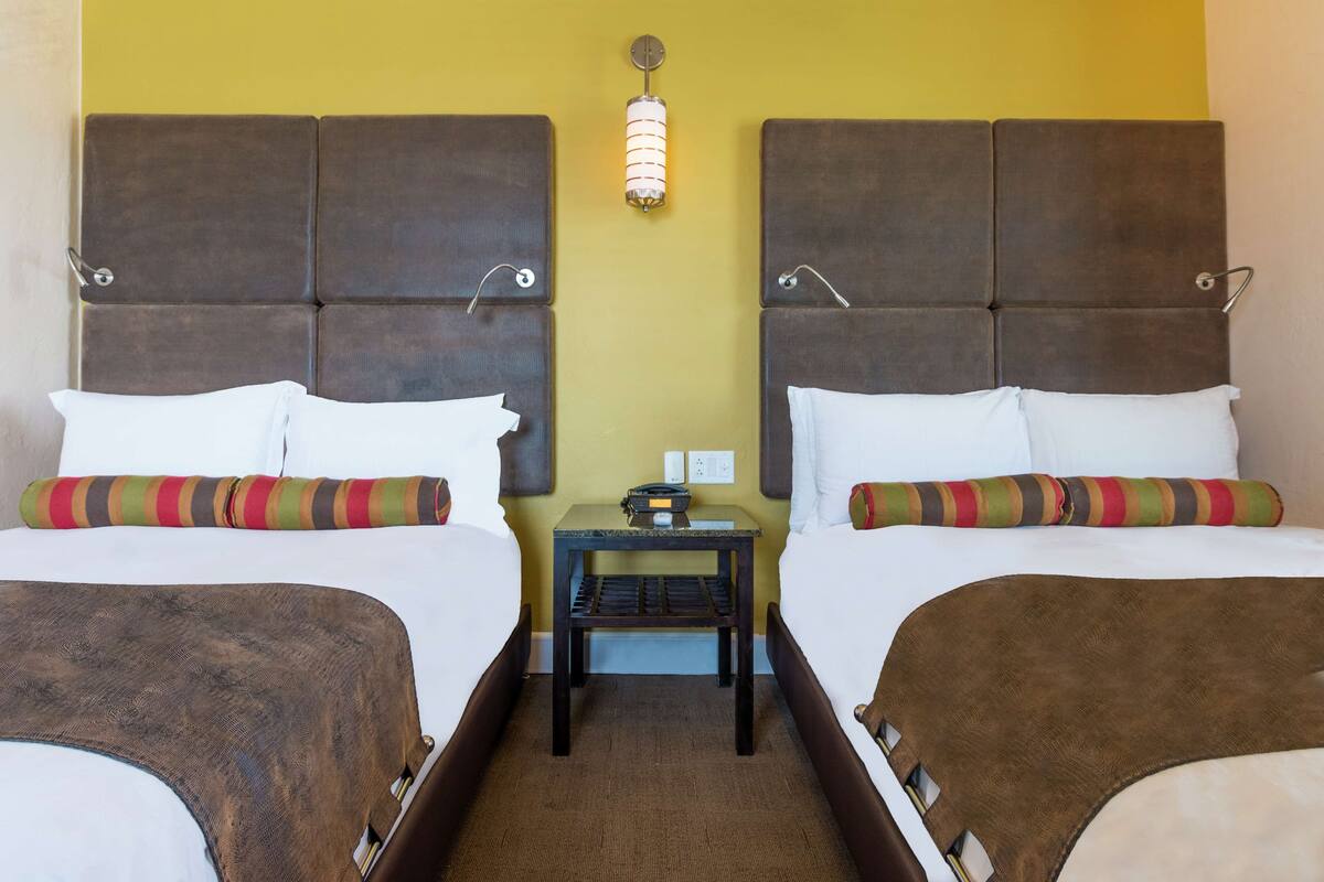 A double room with two beds, each with a headboard, a nightstand, and a lamp between the beds.