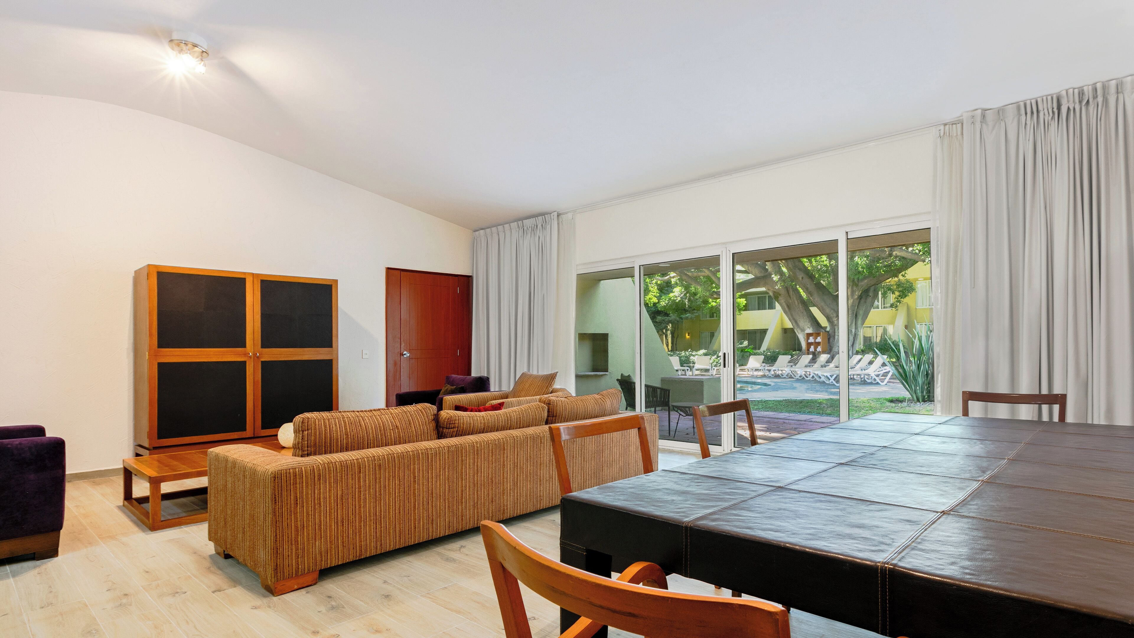 A modern living room with a sofa, a dining table, and a view of a courtyard with outdoor seating.