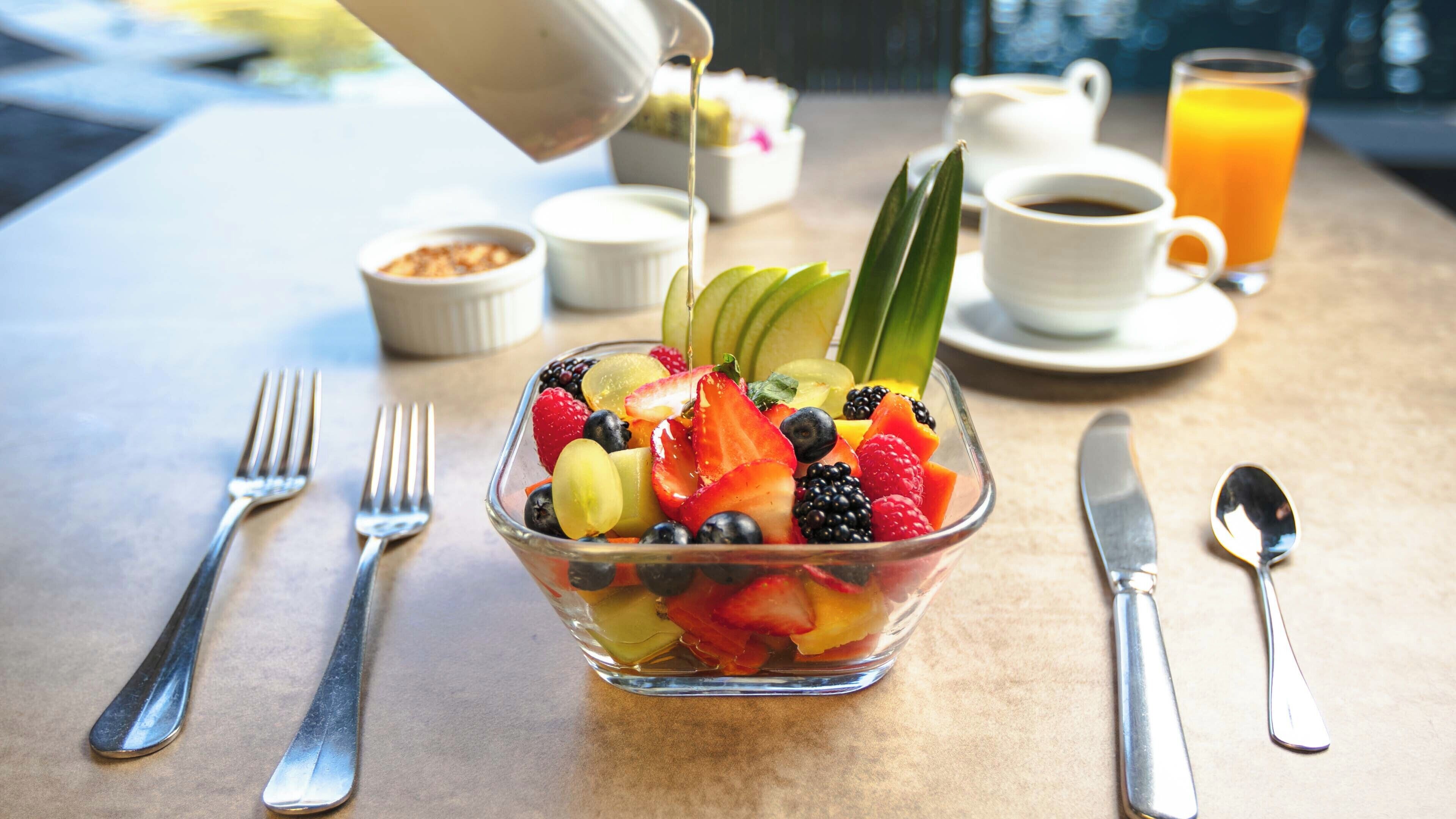 A breakfast setting with a fruit bowl, coffee cup, and orange juice on a table.