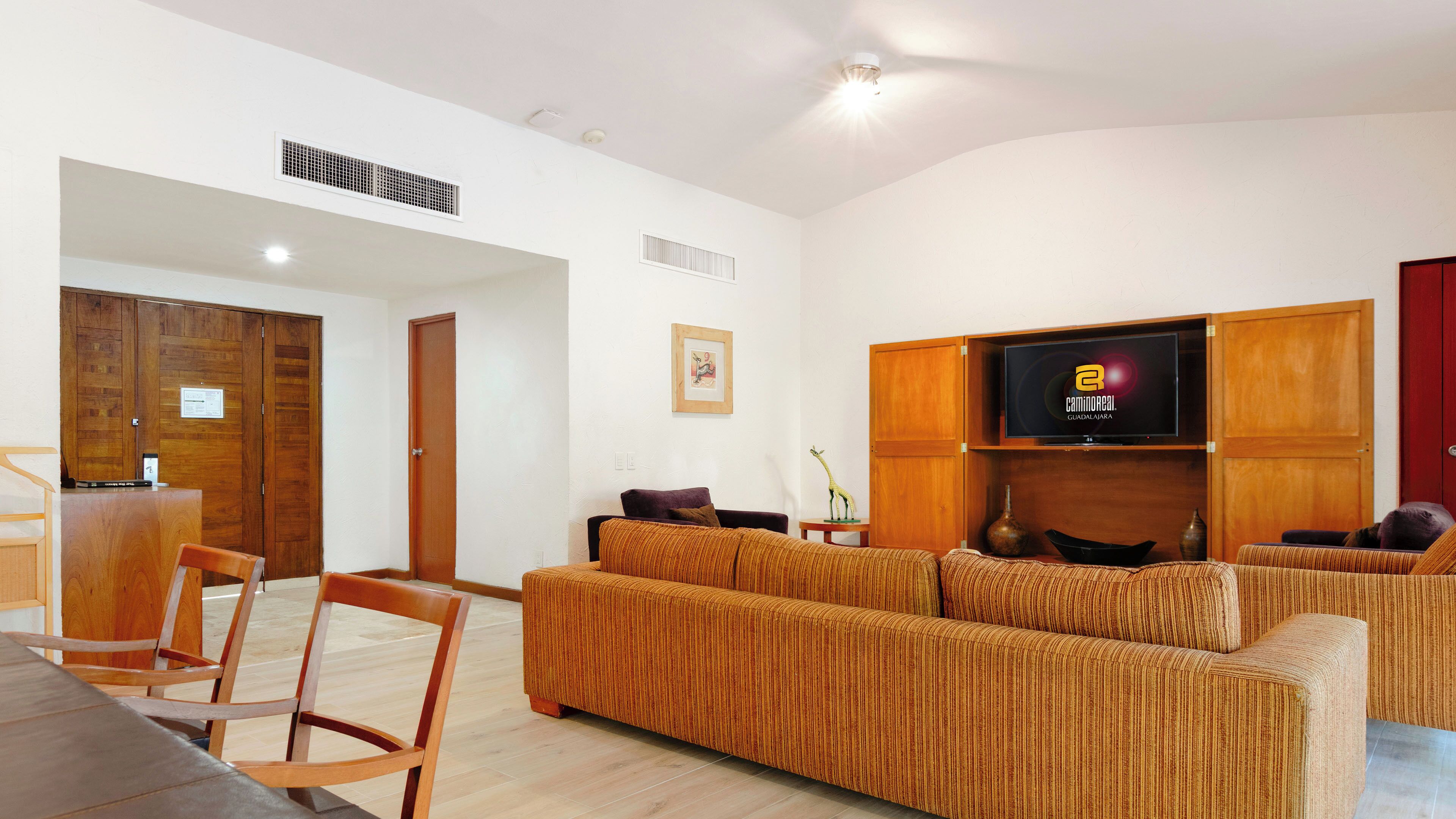 Una sala de estar moderna con un amplio sofá, un televisor fijado a una pared de madera y una puerta de madera al fondo.