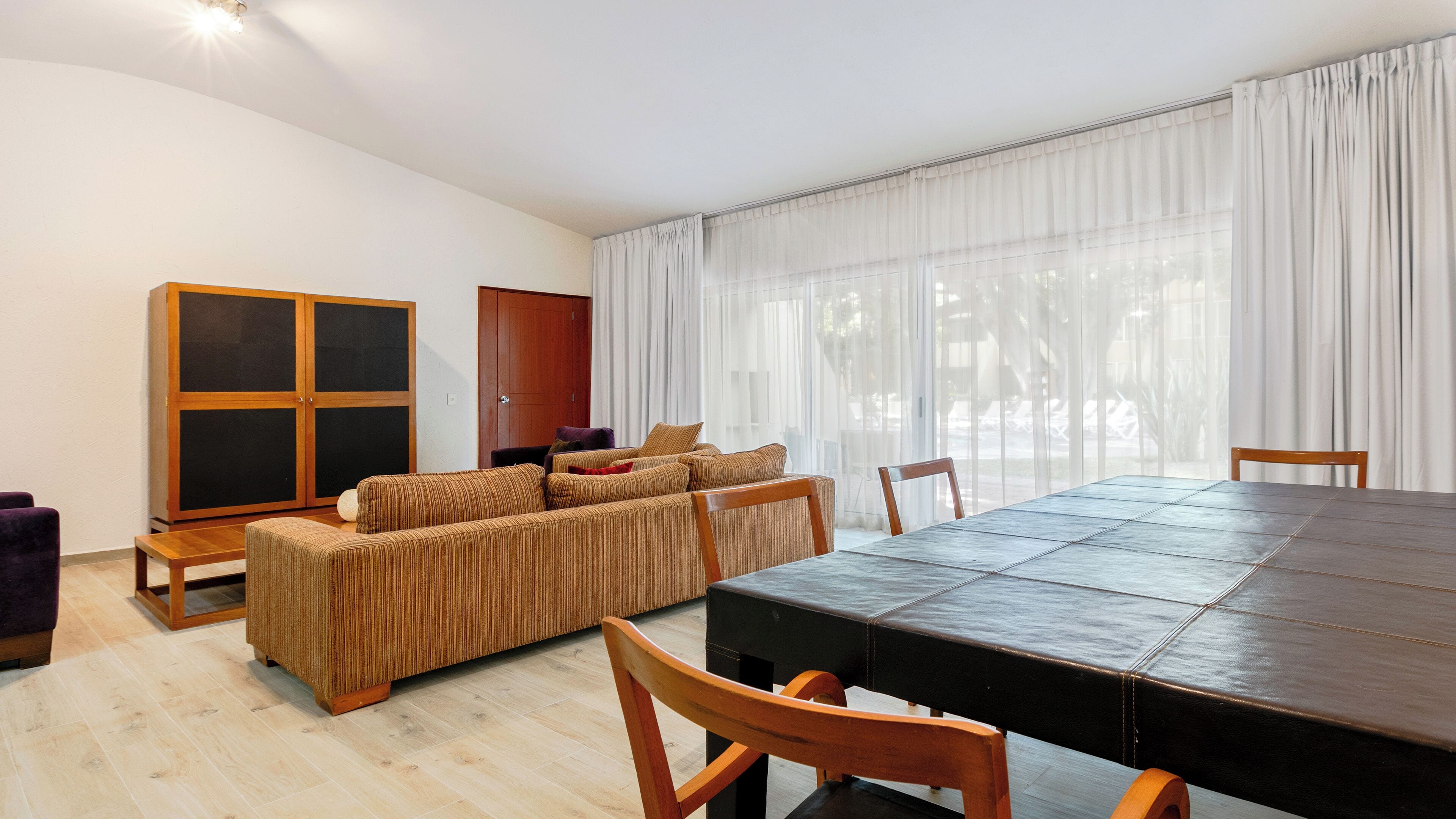 A spacious living area with a large dining table, a sofa set, and a wardrobe.