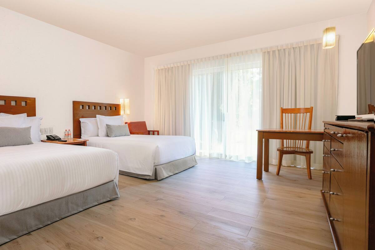 Ein Hotelzimmer mit zwei Betten, einem Schreibtisch, einem Sessel und einem Schminktisch.