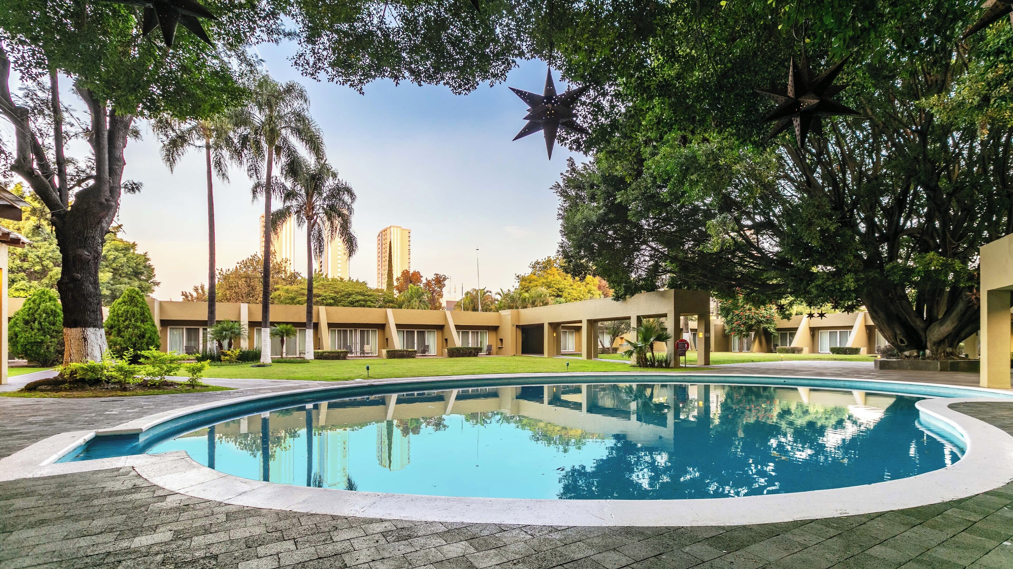 A swimming pool surrounded by palm trees and a building with a modern design.