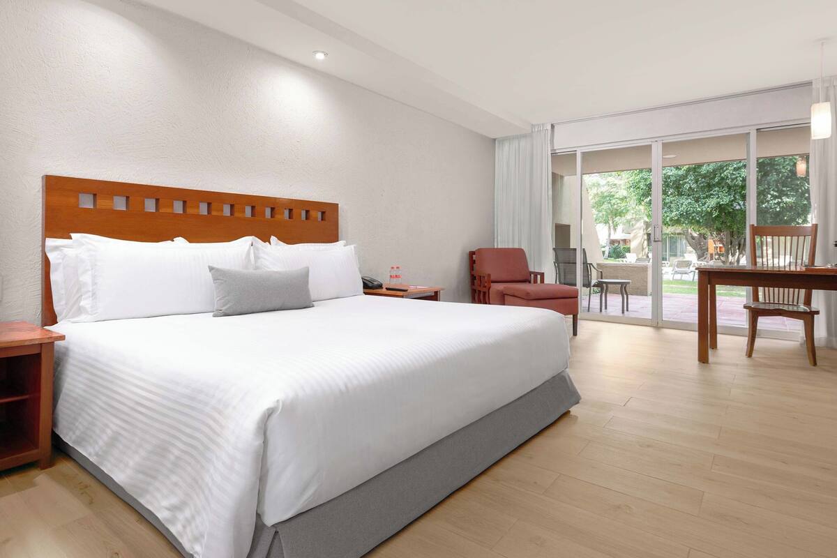 Ein Hotelzimmer mit einem großen Bett, einem Schreibtisch, einem Stuhl und Blick ins Freie.