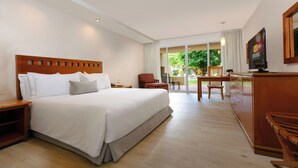 Ein Hotelzimmer mit einem großen Bett, einem Holzkopfstück, einem Schreibtisch mit Stuhl, einem Fernseher und Blick ins Freie.