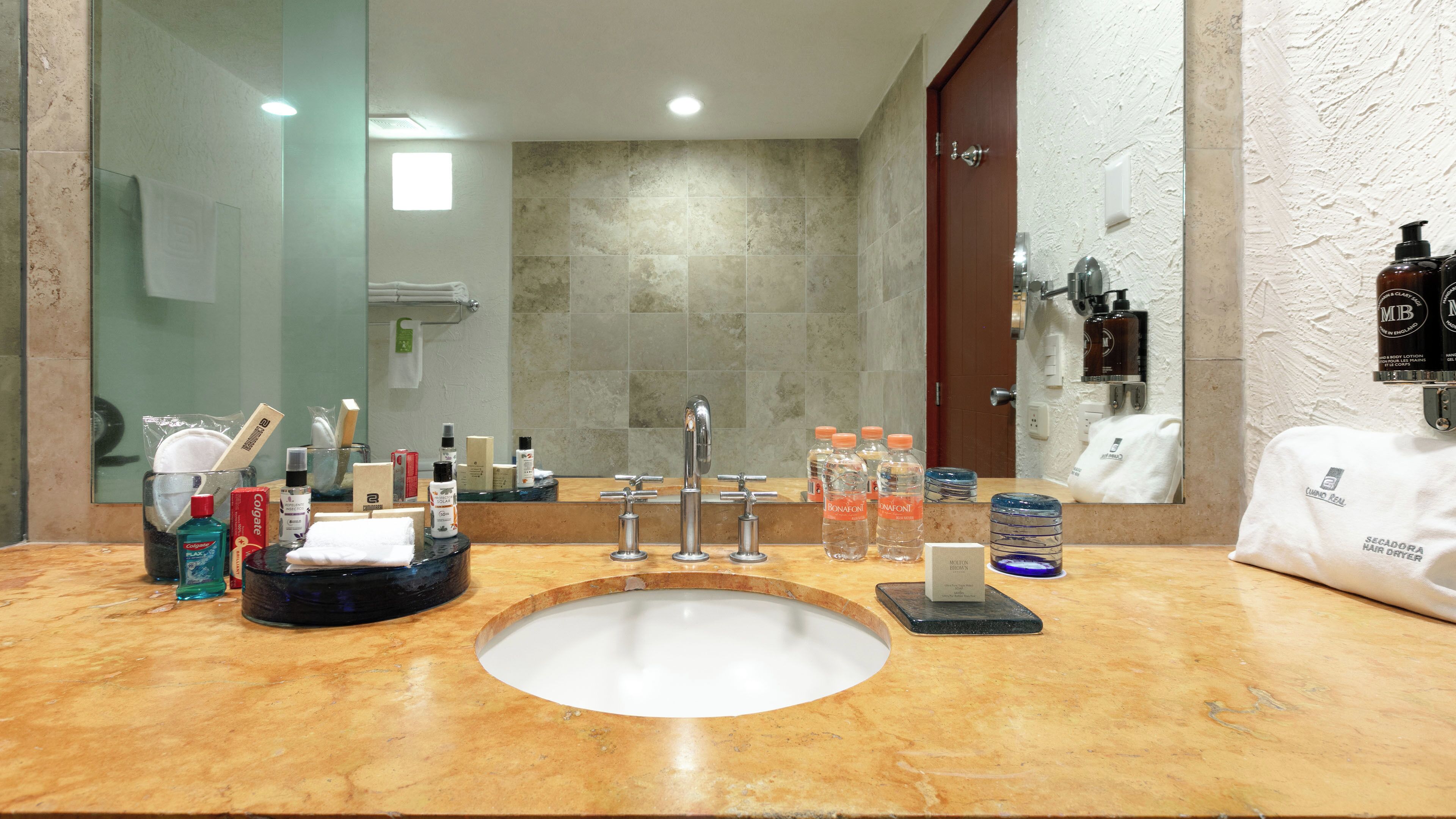 A bathroom with a marble sink, multiple faucets, a mirror, toiletries, and a towel rack.