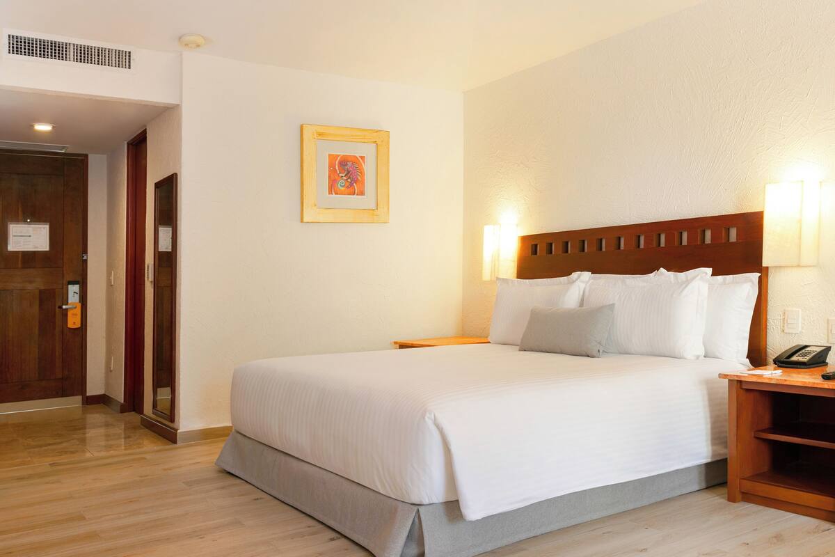 Ein Hotelzimmer mit Bett, Holz-Kopfteil, Nachttischen und einer Wandleuchte.