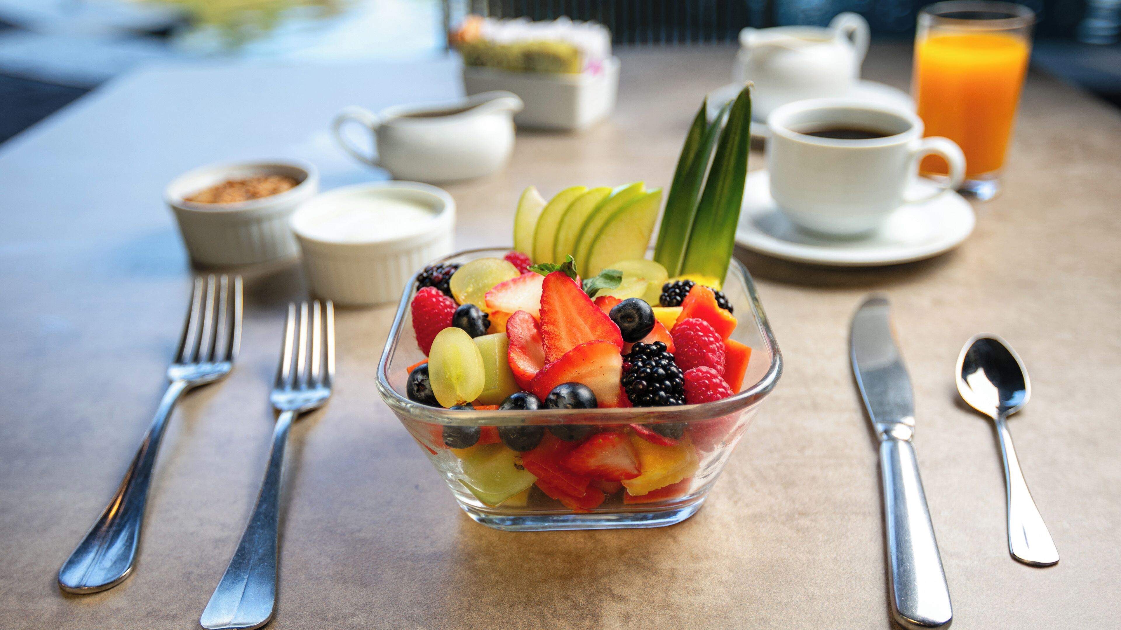 Une table mise pour le petit-déjeuner, avec un panier de fruits, du café et du thé.
