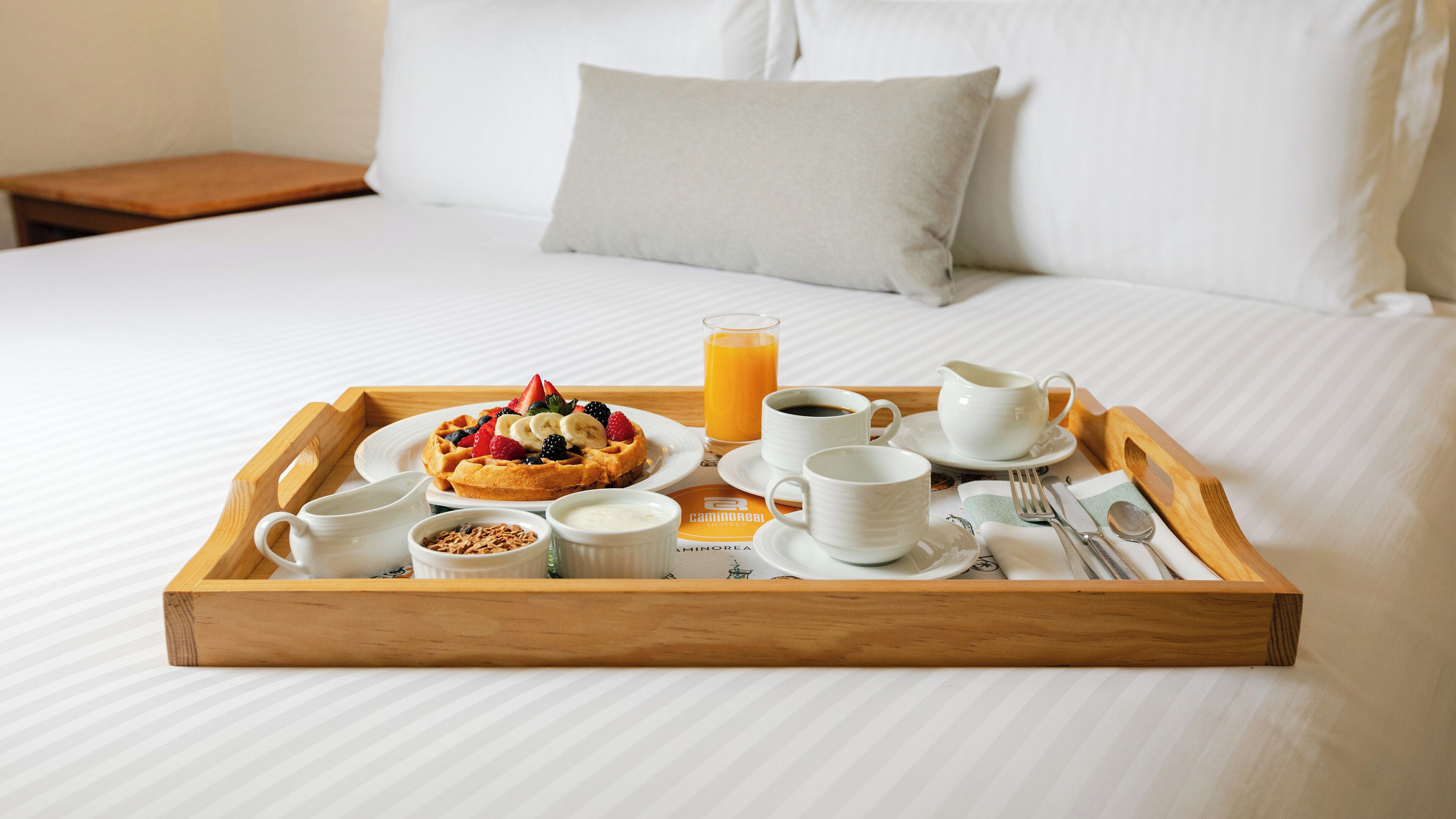 A breakfast tray with waffles, fruit, juice, and coffee on a bed.